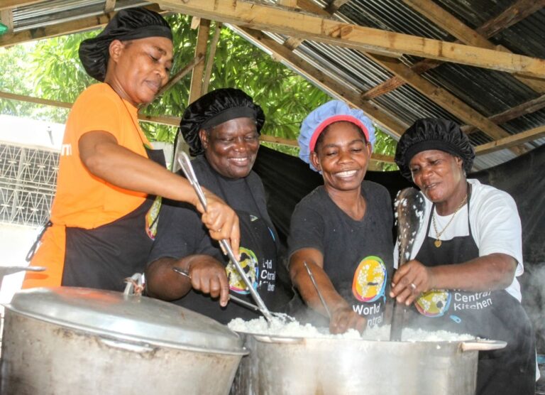 Four World Central Kitchen cooks in Haiti smile as they stir large pots of steaming rice.